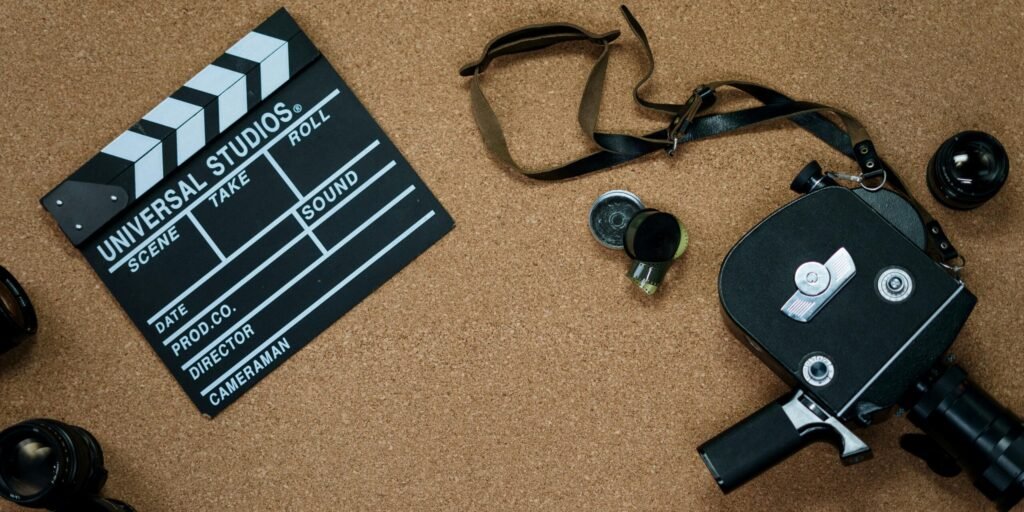 Flat lay of vintage cinema equipment with a film slate and camera on a cork board background.